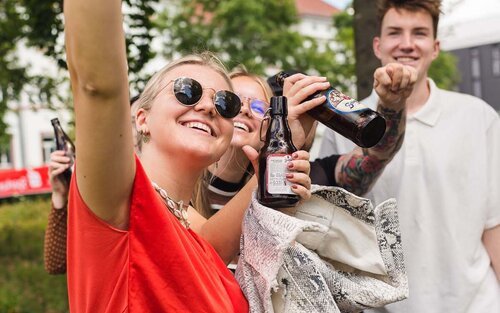 Drei Studierende feiern mit Bierflaschen auf dem Campus