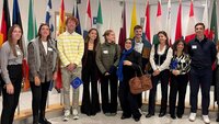 Eine Gruppe von Studierenden im Europäischen Parlament mit Flaggen im Hintergrund