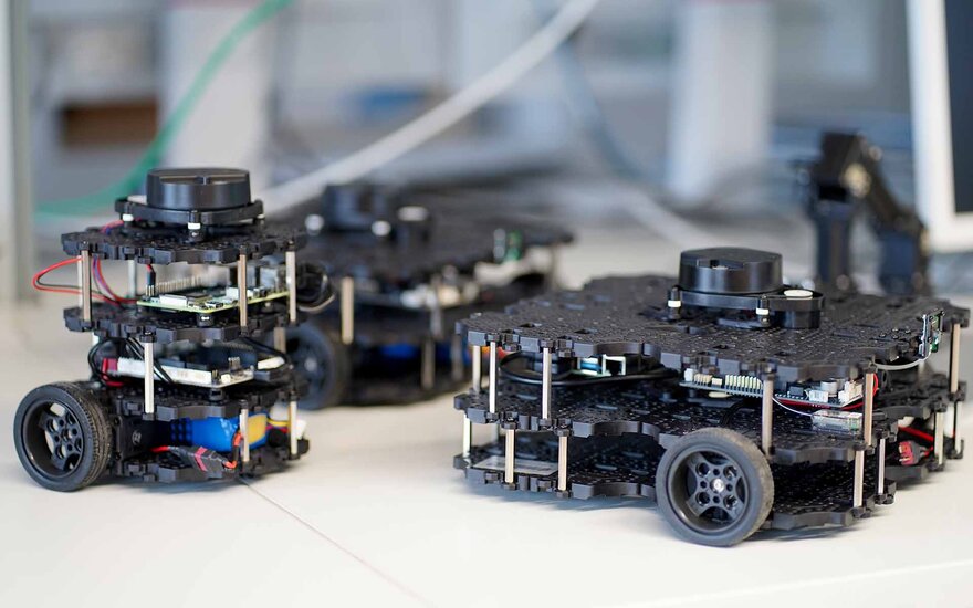 Zwei Roboterlehrplattformen, bestehend aus mehreren schwarzen Kunststoffplatten, die übereinander angeordnet sind und Räder haben