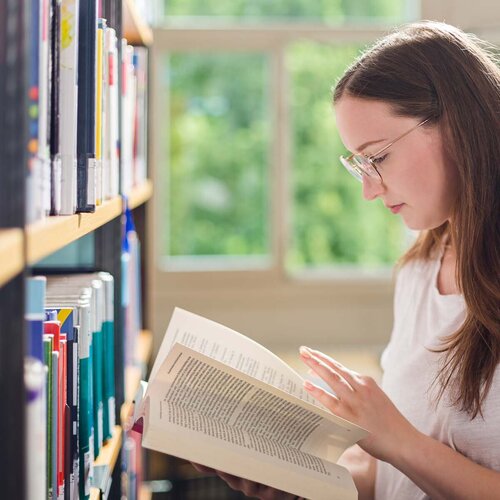 Studentin liest in Buch in der Bibliothek