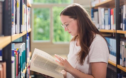 Studentin liest in Buch in der Bibliothek