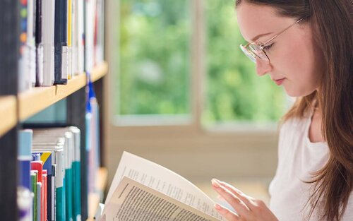 Studentin liest in Buch in der Bibliothek