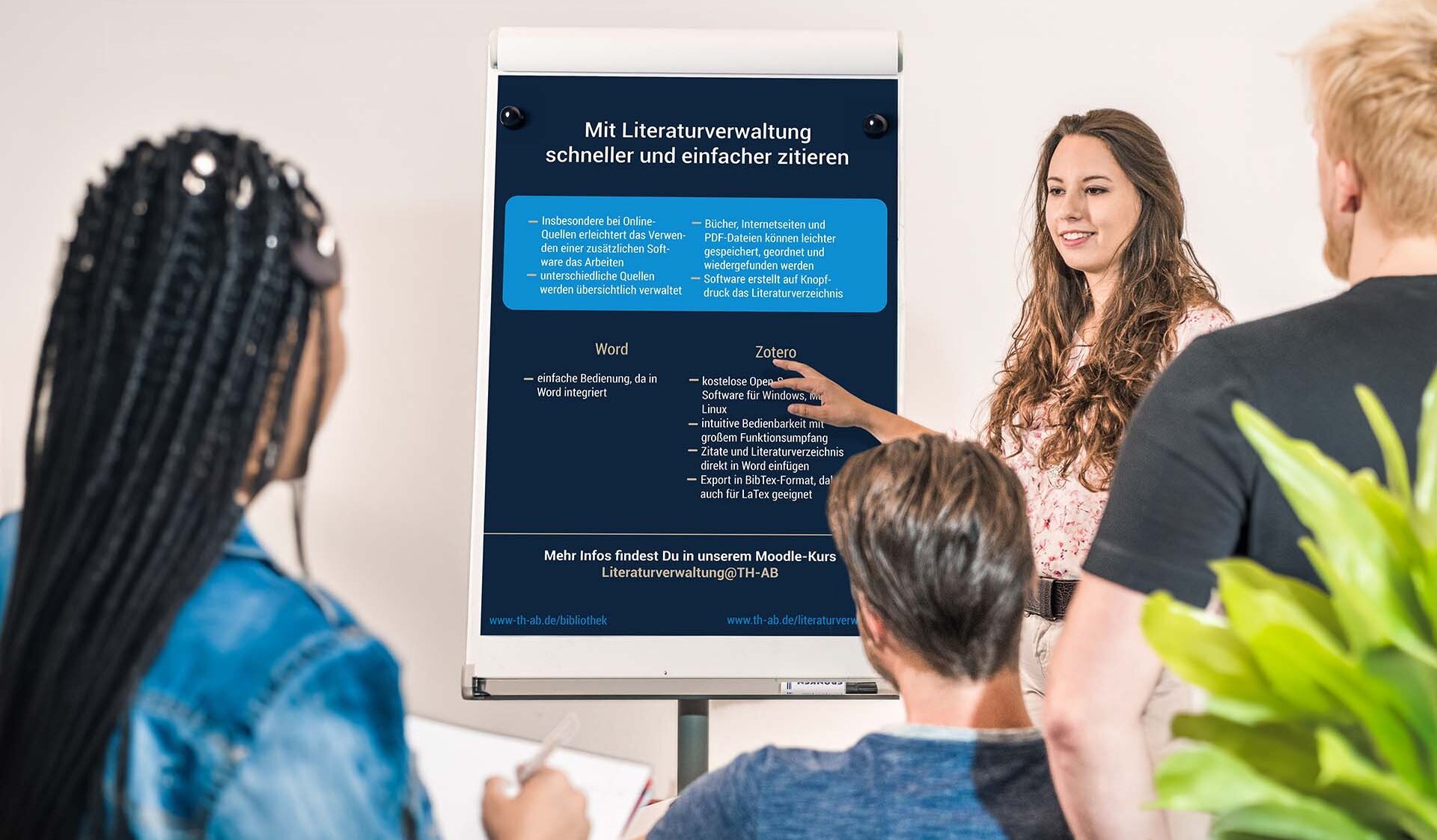 Drei Studierende hören einer Studierende, Referentin, Professorin, Dozentin zu, zeigt auf Flipchart mit Infos zum Zitieren