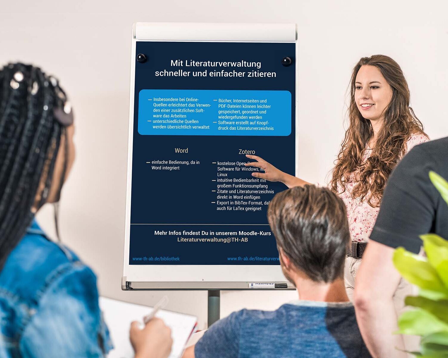 Drei Studierende hören einer Studierende, Referentin, Professorin, Dozentin zu, zeigt auf Flipchart mit Infos zum Zitieren