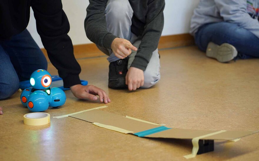 Kinder spielen mit einem mini Roboter auf dem Boden.
