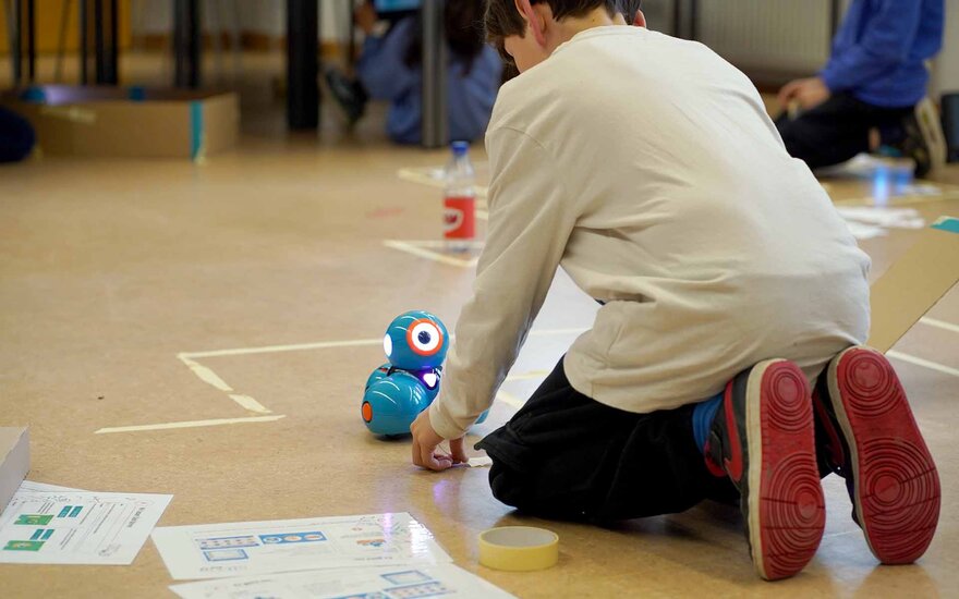 Ein kleiner Junge spielt mit einem Mini Roboter auf dem Boden.