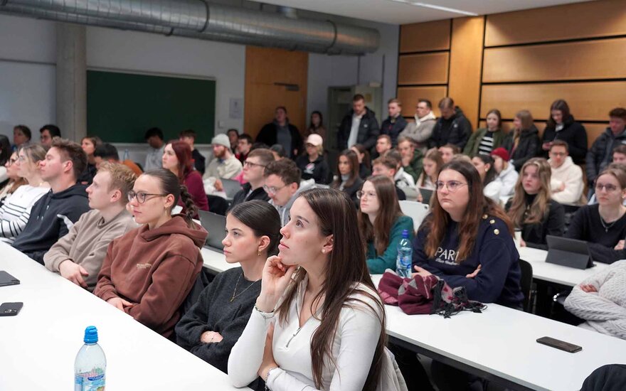 Im Hörsaal in mehreren Reihen sitzende Studierende von vorne während der Live-Schaltung 