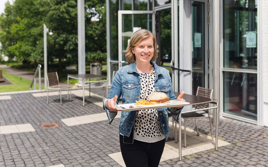 Junge Frau mit Tablett vor der Mensa