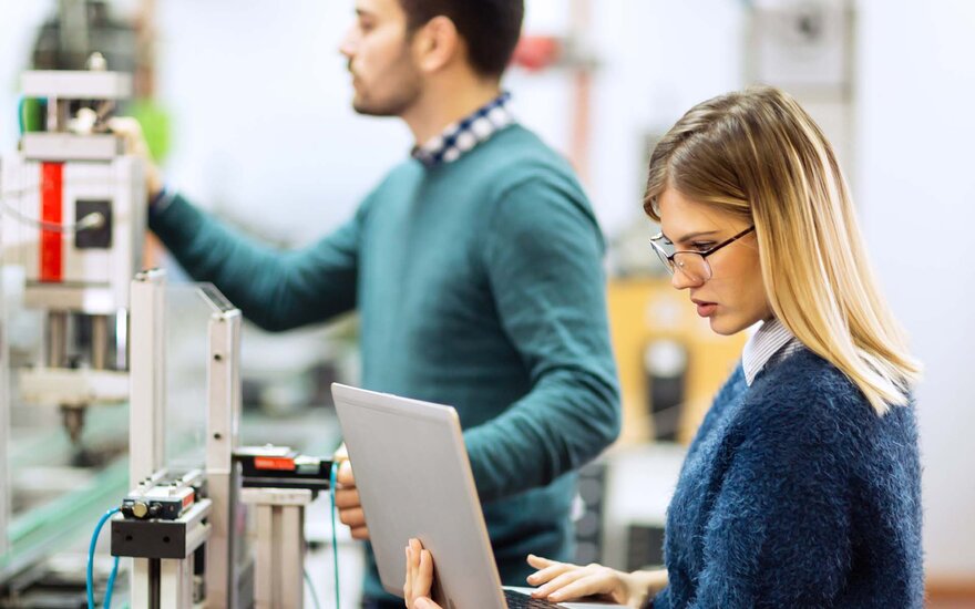 EIne Frau und ein Mann arbeiten mit Laptop an einer elektronischen Vorrichtung