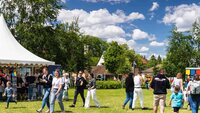 Besucherinnen und Besucher laufen über die Campuswiese zwischen verschiedenen Ständen vor strahlend blauem Himmel