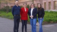 Drei Professorinnen und ein Professor der Fakultät Gesundheitswissenschaften stehen nebeneinander auf dem Campus vor einem Gebäude mit rotbraunen Backsteinen