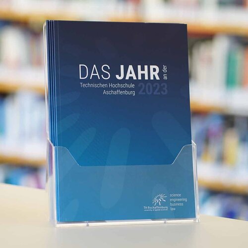 Blaues Cover des Jahresberichtes 2023 vor Bücherregal im Hintergrund