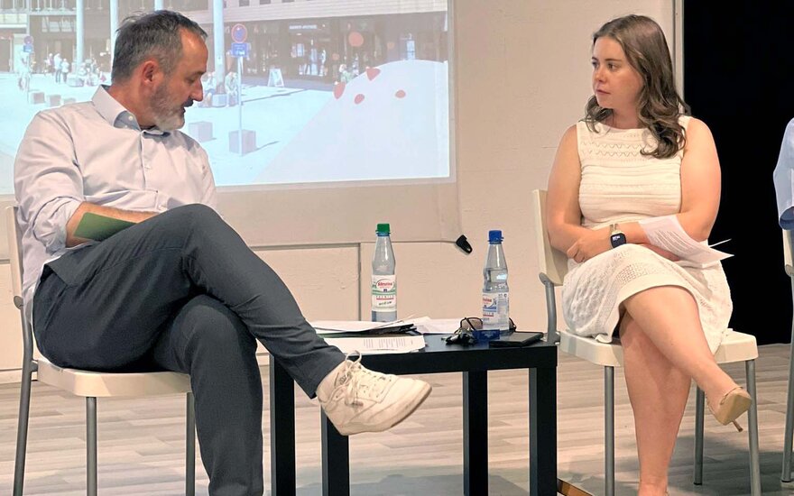 Ein Mann und eine Frau sitzen im Rahmen einer Podiumsdiskussion nebeneinander auf einer Bühne und unterhalten sich.