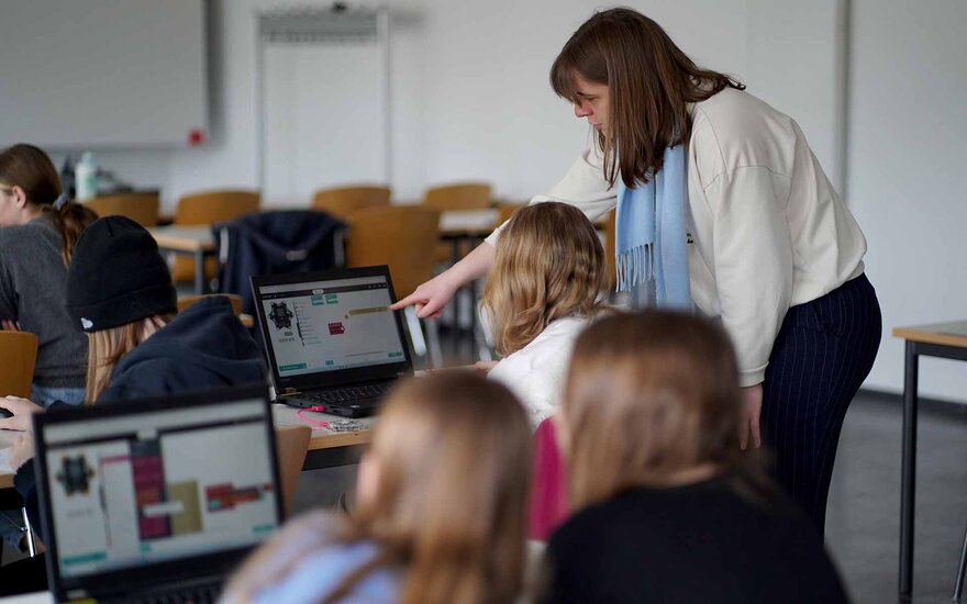 Mädchen sitzen an Laptops und bekommen etwas gezeigt.