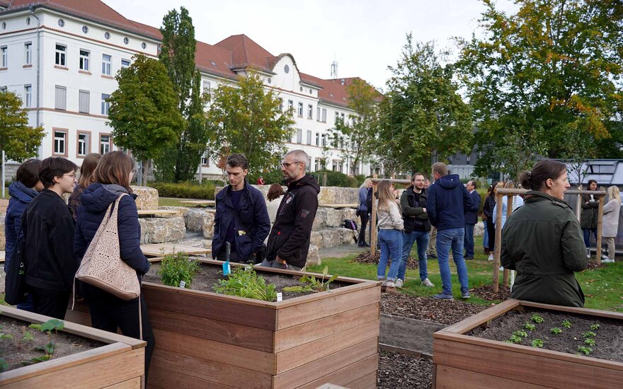 Viele Hochschulangehörige stehen um die Hochbeete herum und an Stehtischen und schauen sich den neuen Garten an.