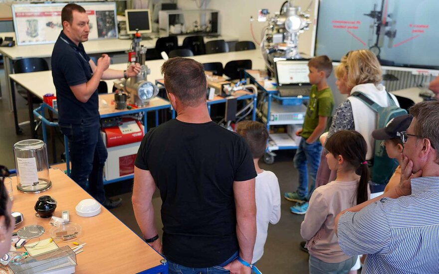 Angehöriger der Fakultät Ingenieurwissenschaften und Informatik führt Besuchern im Labor eine Maschine vor.