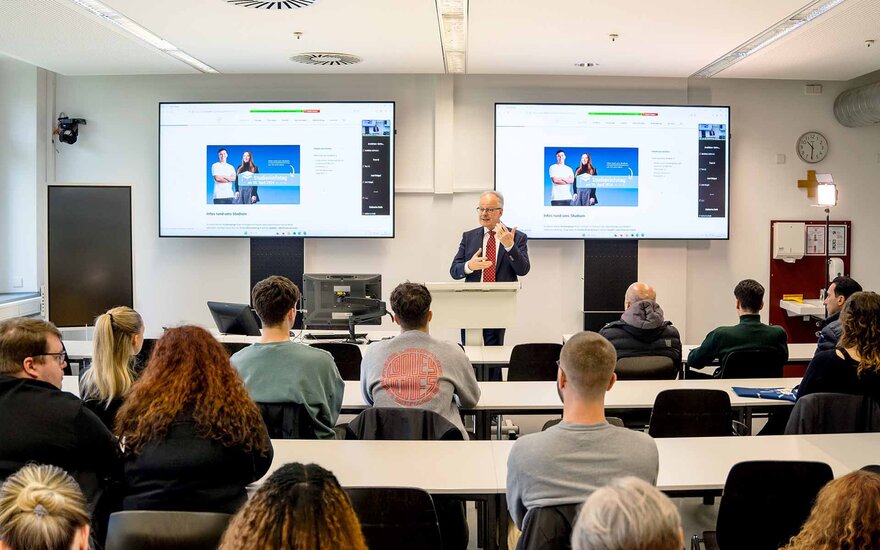 Professor Webersinke hält in einem Hörsaal mit zwei Screens einen Vortrag.