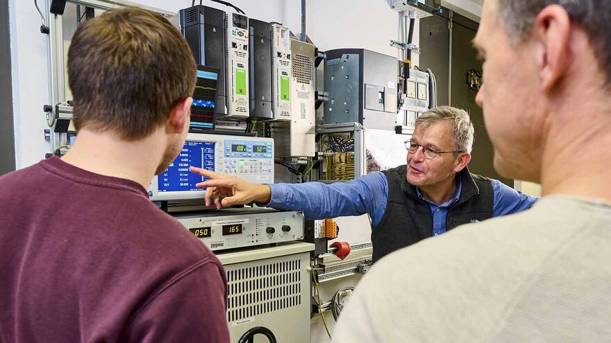 Ein Professor erklärt seinen Mitarbeiterin elektrische Spannungen am Oszilloskop.