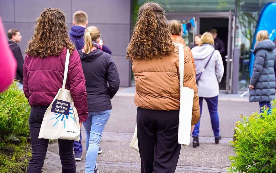 Studieninteressierte laufen auf ein Gebäude der Hochschule mit geöffneter Tür zu.