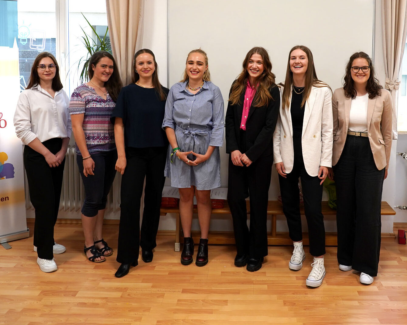 Sieben junge Frauen in einer Reihe, lächeln in die Kamera, rechts und links von ihnen Zonta-Roll-Ups