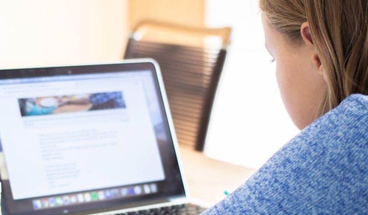 Schülerin arbeitet mit Mäppchen und Laptop an einem Tisch