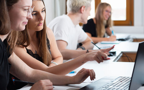 Vier Studierende mit Laptops in Seminarraum von der Seite