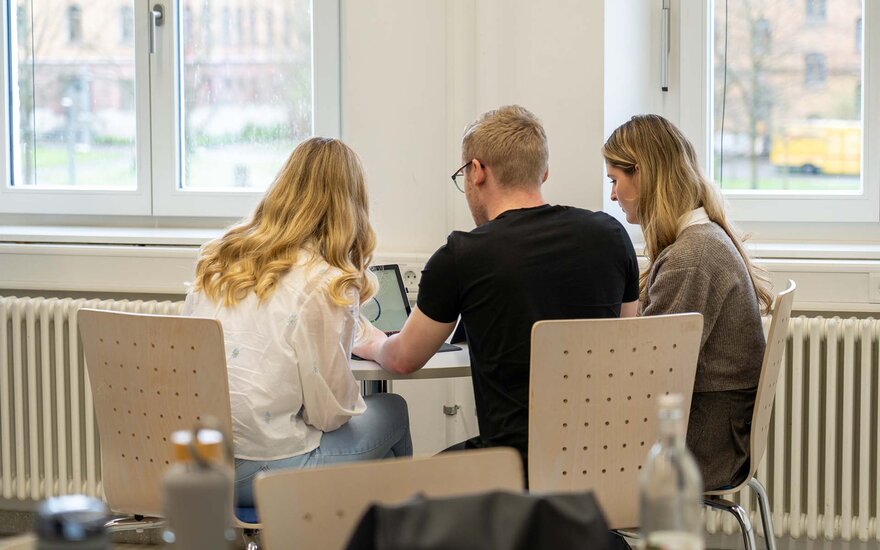 drei Studenten bei der Arbeit an einem Laptop.