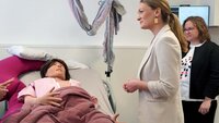 Gesundheitsministerin Judith Gerlach steht im Skills Lab vor einem Bett mit einer lebensgroßen Puppe, die eine schwangere Frau verkörpert, und spricht mit Professorin Hemma Pfeifenberger 