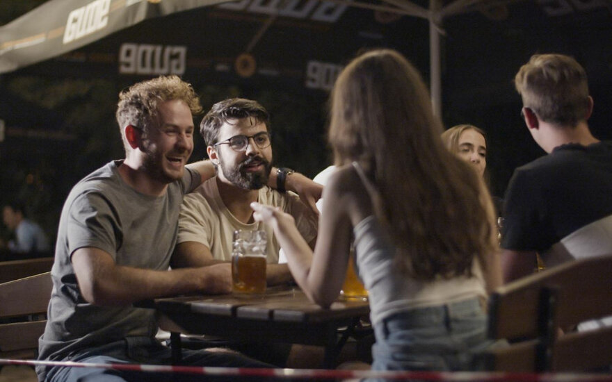 Sechs Studierende Gruppe sitzen zusammen unter Schirm im Biergarten, lachend unterhalten sich, trinken Bier