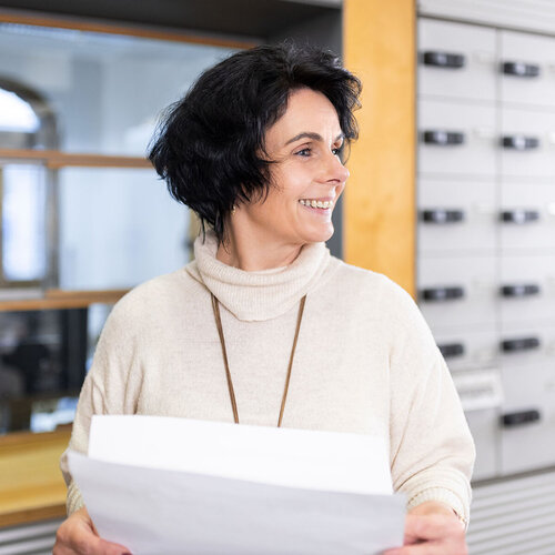 Frau steht vor Postfächern mit Papier in der Hand.