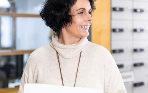 Frau steht vor Postfächern mit Papier in der Hand.