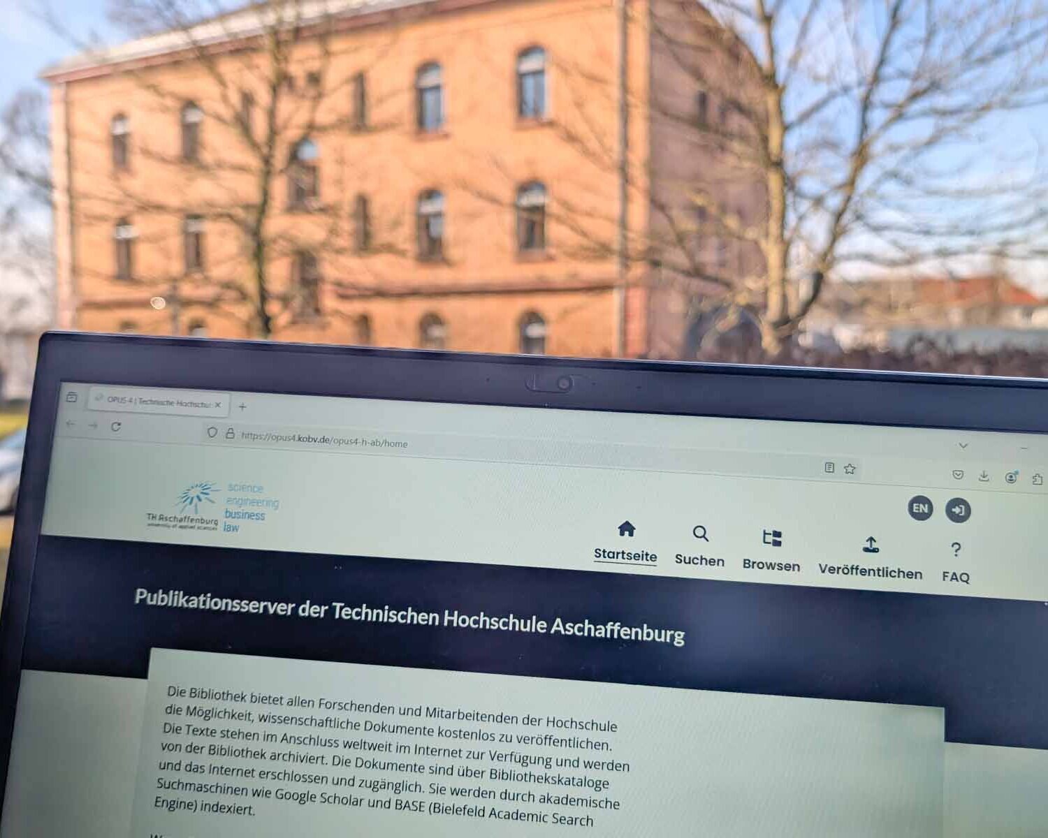 Bildschirm mit Website zum Publikationsserver vor Fenster mit rotem Backsteingebäude der TH