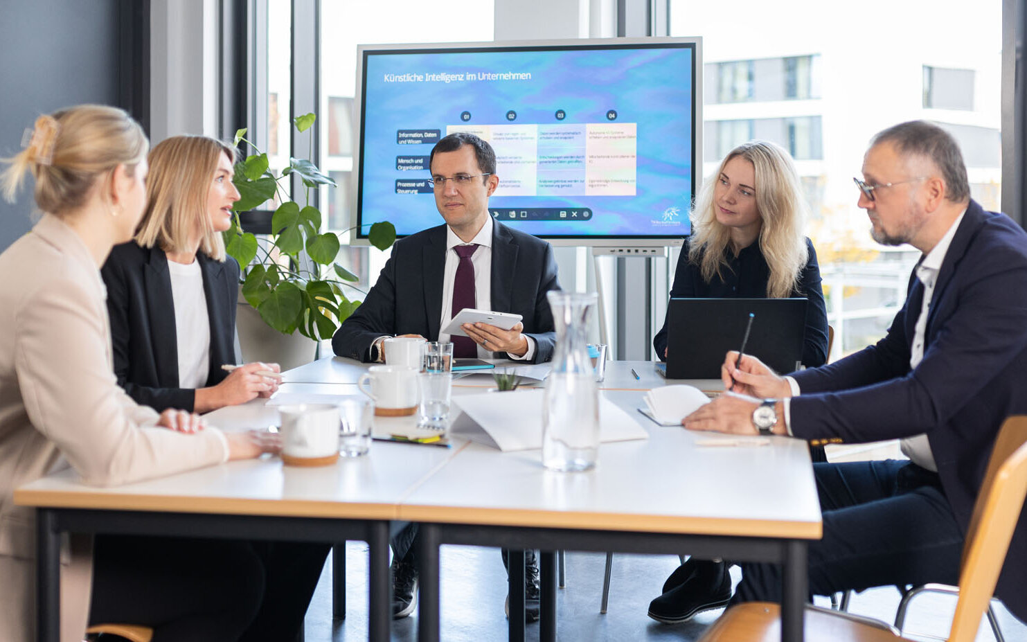 Fünf Personen sitzen an einem Meeting-Tisch 