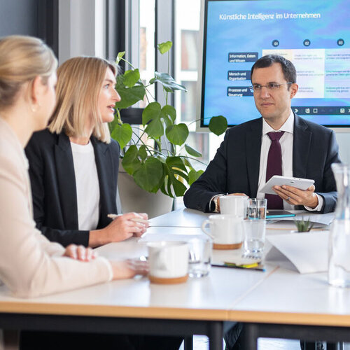 Fünf Personen sitzen an einem Meeting-Tisch 