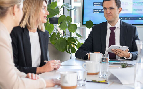 Fünf Personen sitzen an einem Meeting-Tisch 