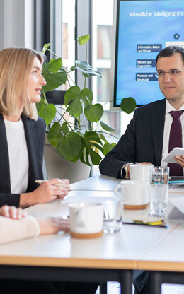 Fünf Personen sitzen an einem Meeting-Tisch 