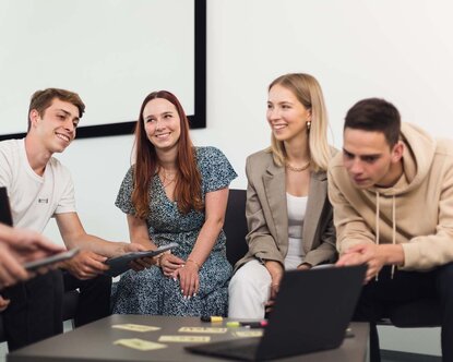 Studierende des Studiengangs SD sitzen mit Laptops und tablets in einem Kreis.