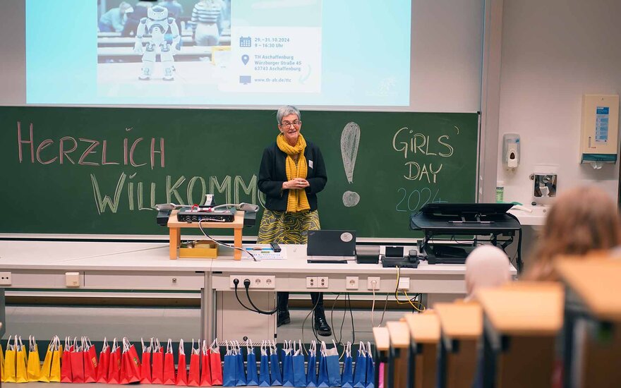 Eine Frau begrüßt die Mädchen des girls Day in eine Vorlesungsraum. 