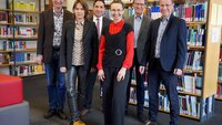 Zwei Professorinnen und vier Professoren stehen nebeneinander vor Bücherregalen in der Bibliothek und lächeln in die Kamera