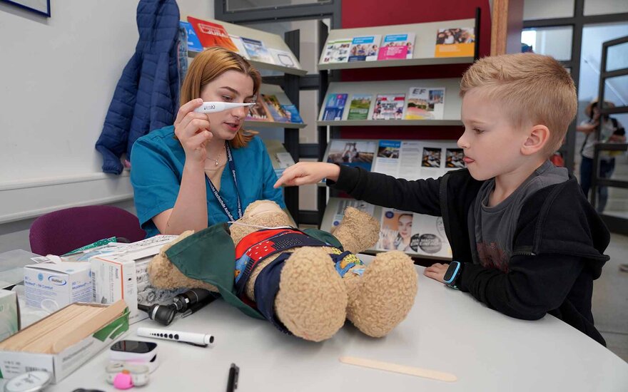 Hebammen Studentin verarztet zusammen mit einem Kind einen Teddybär am Open Campus.