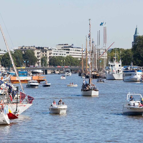 Segelboote auf dem Wasser an einem Hafen. Im Hintergrund ist eine Stadt. 