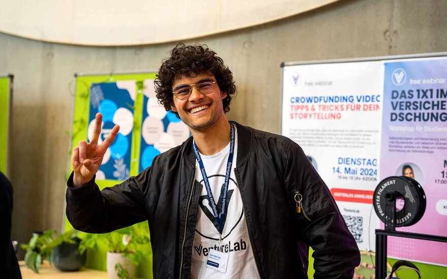 Ein Student aus dem VentureLab hält lächelnd zwei Finger siegessicher in die Höhe.