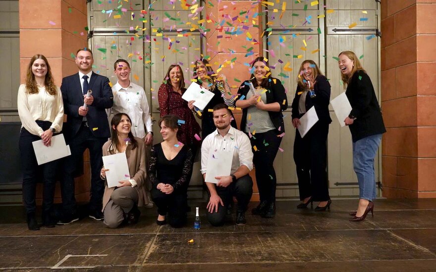 Gruppenfoto der lachenden Absolventinnen und Absolventen, die Konfetti hochwerfen