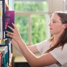 Studentin stellt Buch in Buchregal in der Bibliothek