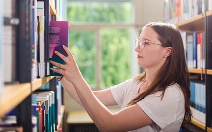 Studentin stellt Buch in Buchregal in der Bibliothek