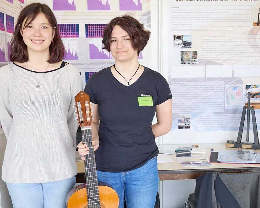 Anna und Susanne stehen nebeneinander und halten eine Gitarre in den Händen