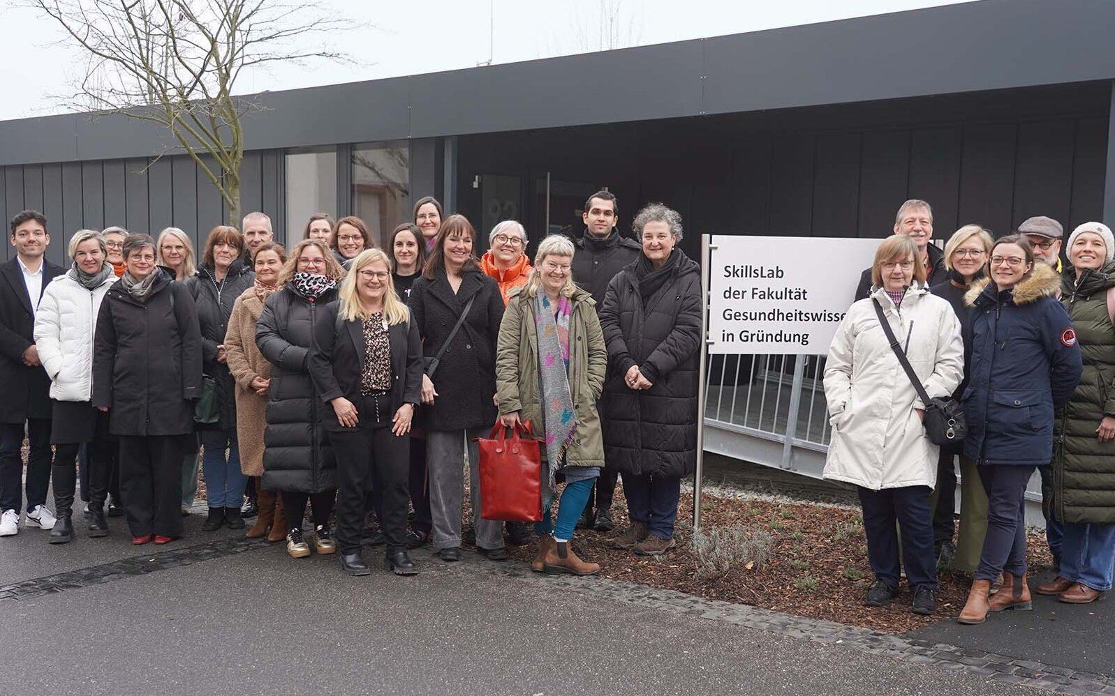 Gruppenfoto der Teilnehmenden vor dem Schild und Container der Fakultät Gesundheitswissenschaften.