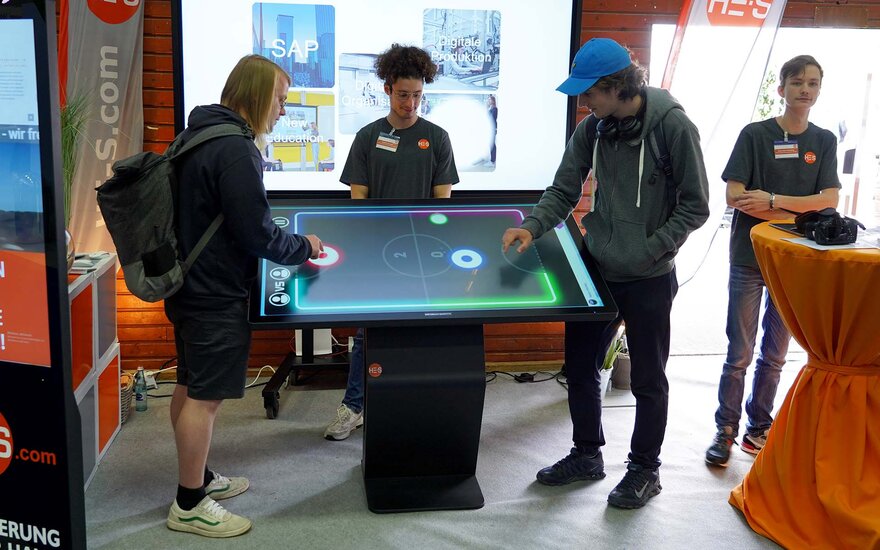 Vier junge Männer stehen um einen Tisch herum, auf dem ein digitales Fußballspiel gespielt werden kann