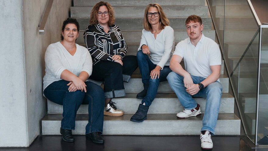 Vier Mitarbeitende sitzen auf einer Treppe