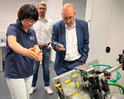 Labormitarbeiterin erklärt dem Gutachter die Arbeit der Forschungsgruppe hinsichtlich der Laser-Lichtführung entlang des Industrie-Roboters